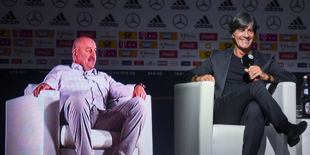 Joachim Löw sitzt auf einem Sessel und lächelt, neben ihm auf einem Sessel das Abbild von Stanislaw Tschertschessow