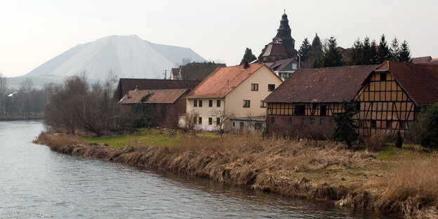 Häuser stehen an einm Fluss, dahinter ist ein Kali-Berg Häuser stehen an einm Fluss, dahinter ist ein Kali-Berg