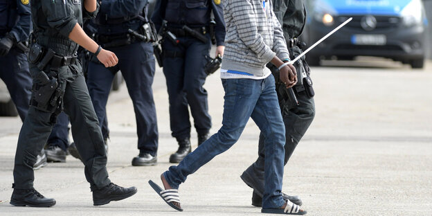 Ein gefesselter Mann wird von maskierten Polizisten abgeführt. Ein gefesselter Mann wird von maskierten Polizisten abgeführt.