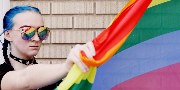 Eine Frau mit blauen Haaren hält energisch eine Regenbogenflagge Eine Frau mit blauen Haaren hält energisch eine Regenbogenflagge
