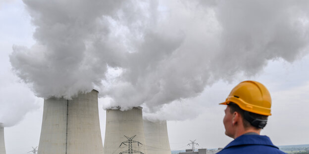 Ein Arbeiter schaut auf dampfende Kühltürme Ein Arbeiter schaut auf dampfende Kühltürme