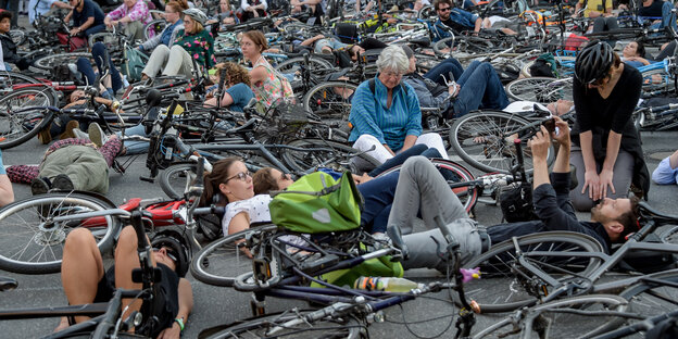 Radfahrer*innen sitzen und liegen auf einer Straßenkreuzung. Radfahrer*innen sitzen und liegen auf einer Straßenkreuzung.