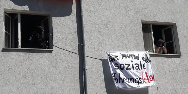 Zwein Menschen hängen ein Transparent au szwei Fenstern Zwein Menschen hängen ein Transparent au szwei Fenstern