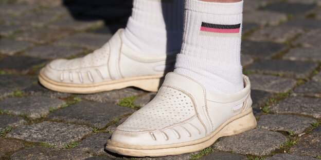zwei Füße in weißen Lederschuhen mit knöchellangen Socken, die eine Deutschlandfahne ziert zwei Füße in weißen Lederschuhen mit knöchellangen Socken, die eine Deutschlandfahne ziert
