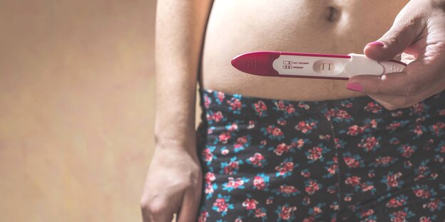 Eine Frau hält einen positiven Schangerschaftstest vor ihren Bauch Eine Frau hält einen positiven Schangerschaftstest vor ihren Bauch