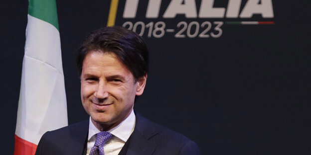Giuseppe Conte steht vor einer italienischen Fahne und lächelt Giuseppe Conte steht vor einer italienischen Fahne und lächelt
