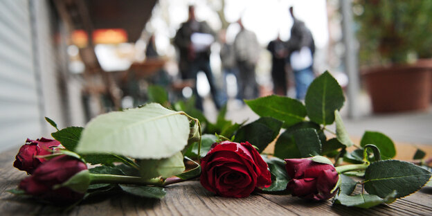 Rosen liegen auf dem Boden, im Hintergrund sind Menschen.