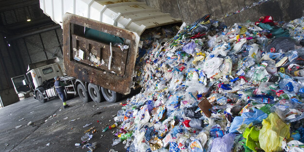 Ein LKW kippt einen Haufen Plastikmüll in einer Halle auf den Boden Ein LKW kippt einen Haufen Plastikmüll in einer Halle auf den Boden