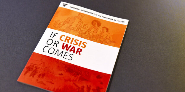 Eine Broschüre in orange, rot und weiß mit der englischsprachigen Aufschrift "Falls Krise oder Krieg kommt" liegt auf einem Tisch Eine Broschüre in orange, rot und weiß mit der englischsprachigen Aufschrift "Falls Krise oder Krieg kommt" liegt auf einem Tisch