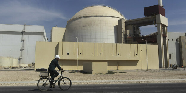 Ein Mann auf einem Fahrrad fährt an einem Atomkraftwerk vorbei Ein Mann auf einem Fahrrad fährt an einem Atomkraftwerk vorbei