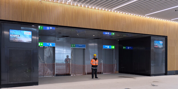 ein Bauarbeiter vor abgesperrten Fahrstühlen in einem leeren Flughafengebäude ein Bauarbeiter vor abgesperrten Fahrstühlen in einem leeren Flughafengebäude