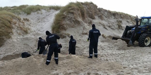 Sechs Polizisten mit Schaufeln und Bagger graben in einer Düne Sechs Polizisten mit Schaufeln und Bagger graben in einer Düne