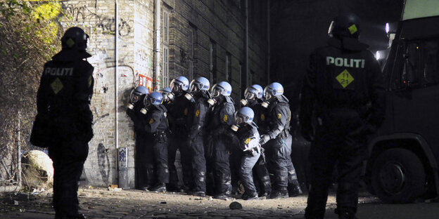 Polizisten in voller Montur stehen an einer Mauer Polizisten in voller Montur stehen an einer Mauer