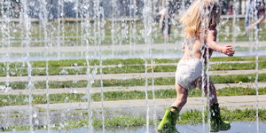 Ein Kind in einer Windel und mit Gummistiefeln rennt durch einen Springbrunnen