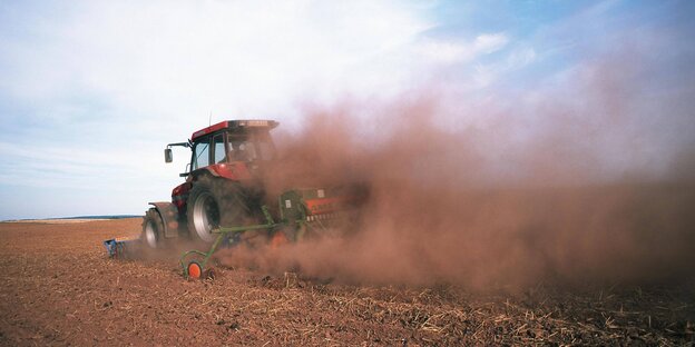 Ein Traktor fährt, eingehüllt in einer Staubwolke, über ein Feld Ein Traktor fährt, eingehüllt in einer Staubwolke, über ein Feld