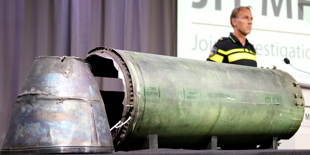 Auf einem Tisch werden Teile einer Rakete präsentiert, im Hintergrund ein Schild mit der Aufschrift MH17 Auf einem Tisch werden Teile einer Rakete präsentiert, im Hintergrund ein Schild mit der Aufschrift MH17