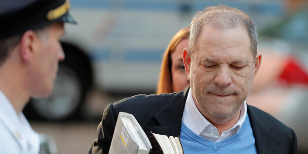Harvey Weinstein neben einem Polizisten. Er trägt Bücher in der rechten Hand Harvey Weinstein neben einem Polizisten. Er trägt Bücher in der rechten Hand