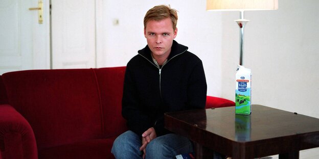 Ein jungen Mann sitzt auf einem roten Sofa, auf dem Tisch neben ihm steht ein Milchkarton Ein jungen Mann sitzt auf einem roten Sofa, auf dem Tisch neben ihm steht ein Milchkarton