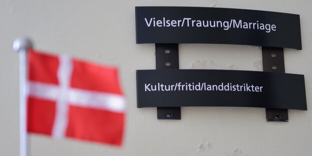 EIne Fahne (weißes Kreuz auf rotem Grund) vor einem Behördenwegweiser. EIne Fahne (weißes Kreuz auf rotem Grund) vor einem Behördenwegweiser.