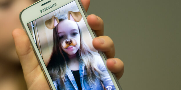 Auf einem Handy sieht man ein Mädchen mit Hundeohren und -nase Auf einem Handy sieht man ein Mädchen mit Hundeohren und -nase