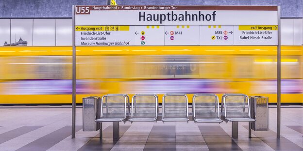 U-Bahnstation, im Mittelpunkt eine Sitzreihe, dahinter ein gelber U-Bahnzug, der schnell ein- oder abfährt U-Bahnstation, im Mittelpunkt eine Sitzreihe, dahinter ein gelber U-Bahnzug, der schnell ein- oder abfährt