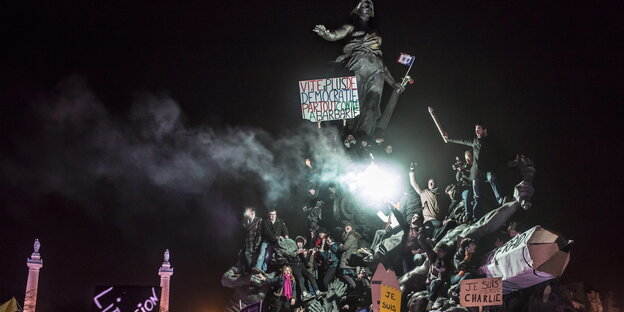 Menschen demonstrieren mit Plakaten auf einer Statue in Paris gegen die Anschläge im Jahr 2015 Menschen demonstrieren mit Plakaten auf einer Statue in Paris gegen die Anschläge im Jahr 2015
