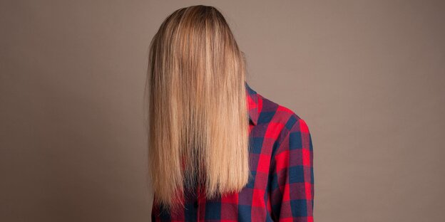 Einer Person mit rot-blau kariertem Hemd hängen die langen Haare vor dem Gesicht Einer Person mit rot-blau kariertem Hemd hängen die langen Haare vor dem Gesicht