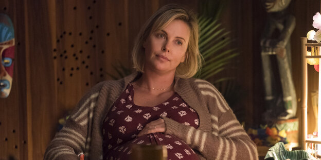 Schauspielerin Charlize Theron sitzt im Film als Hochschwangere auf einem Stuhl und hat ihre Hand auf ihrem Bauch. Schauspielerin Charlize Theron sitzt im Film als Hochschwangere auf einem Stuhl und hat ihre Hand auf ihrem Bauch.