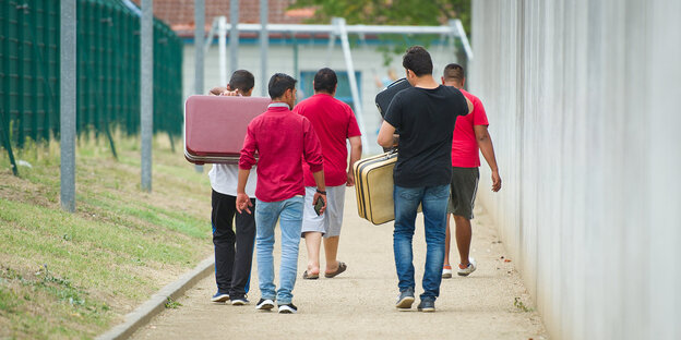 Flüchtlinge laufen mit Koffern bepackt auf einem Weg einer Erstaufnahmeeinrichtung für Flüchtlinge Flüchtlinge laufen mit Koffern bepackt auf einem Weg einer Erstaufnahmeeinrichtung für Flüchtlinge