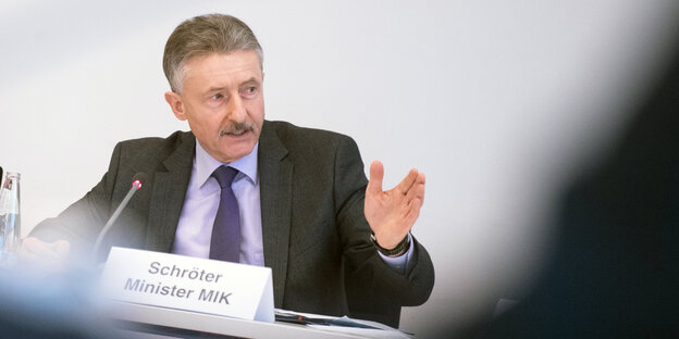 Ein Mann sitzt und gestikuliert mit der linken Hand Ein Mann sitzt und gestikuliert mit der linken Hand