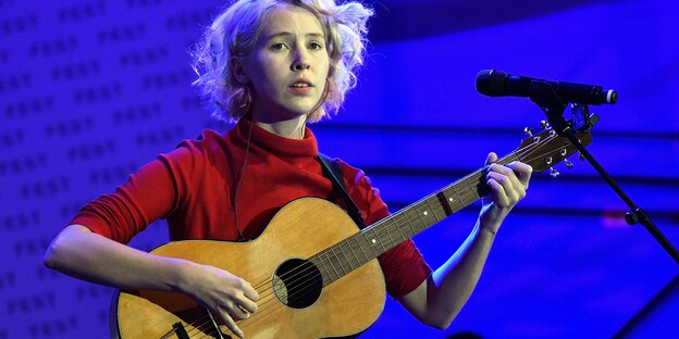 Eine Frau steht mit einer Gitarre auf einer Bühne Eine Frau steht mit einer Gitarre auf einer Bühne