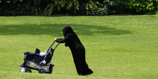 Eine Person in einer Burka schiebt einen Kinderwagen Eine Person in einer Burka schiebt einen Kinderwagen