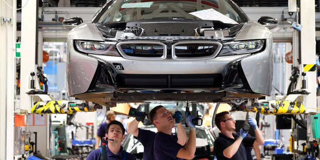 Arbeiter schrauben an einem Auto, das über ihnen hängt herum Arbeiter schrauben an einem Auto, das über ihnen hängt herum