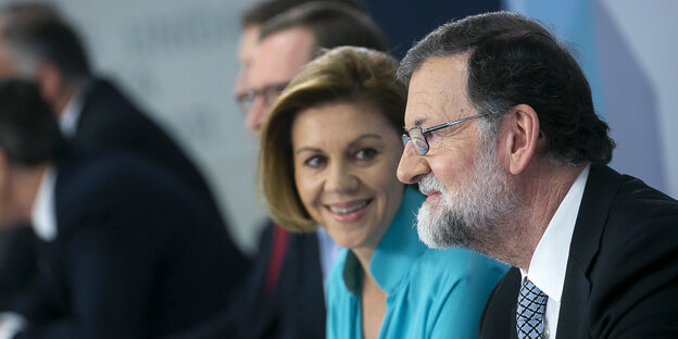Rajoy guckt sinnend vor sich hin, eine Frau guckt lächelnd zu ihm rüber Rajoy guckt sinnend vor sich hin, eine Frau guckt lächelnd zu ihm rüber