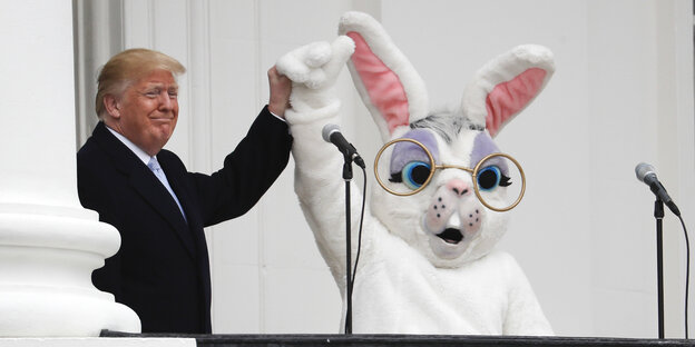 Trump hält im Weißen Haus die Hand eines Menschen im weißen Osterhasenkostüm hoch. Trump hält im Weißen Haus die Hand eines Menschen im weißen Osterhasenkostüm hoch.