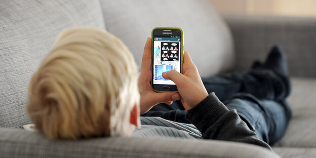 Ein Kind liegt auf einem Sofa und blickt auf ein Handy Ein Kind liegt auf einem Sofa und blickt auf ein Handy