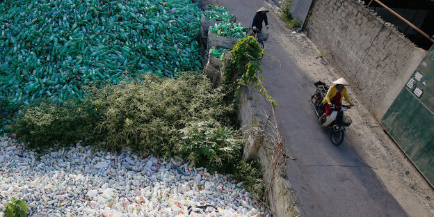 Zwei Vietnamesinnen fahren auf einem Roller an Plastikbergen vorbei Zwei Vietnamesinnen fahren auf einem Roller an Plastikbergen vorbei
