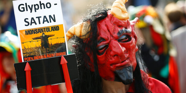 Ein als Teufel kostümierter Aktivist protestiert mit dem Schild "GlyphoSATAN" vor der Bayer-Konzernzentrale gegen die Fusion mit Monsanto Ein als Teufel kostümierter Aktivist protestiert mit dem Schild "GlyphoSATAN" vor der Bayer-Konzernzentrale gegen die Fusion mit Monsanto
