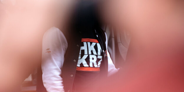 Durch ein von Hände gebildetes Loch ist en T-Shirt mit der Aufschrift „HKNKRZ“ zu sehen Durch ein von Hände gebildetes Loch ist en T-Shirt mit der Aufschrift „HKNKRZ“ zu sehen