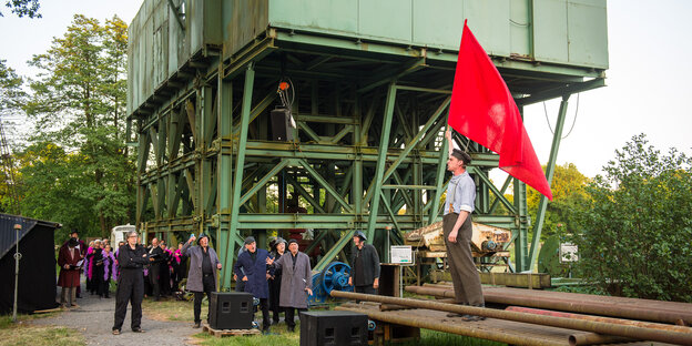 Ein Mann steht vor einer Industrieanlage und hält eine rote Fahne in die Luft Ein Mann steht vor einer Industrieanlage und hält eine rote Fahne in die Luft