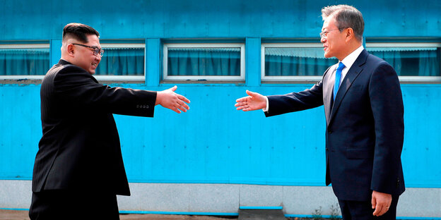 Kim Jong und und Moon Jae In gehen mit ausgestrecken Händen aufeinander zu. Kim Jong und und Moon Jae In gehen mit ausgestrecken Händen aufeinander zu.