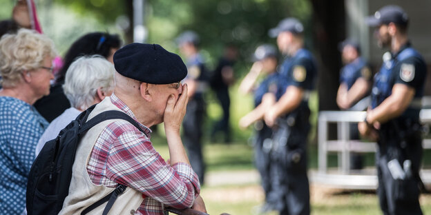 Ein Mann lehnt an einem Absperrgitter und hält sich die Hand vor den Mund Ein Mann lehnt an einem Absperrgitter und hält sich die Hand vor den Mund