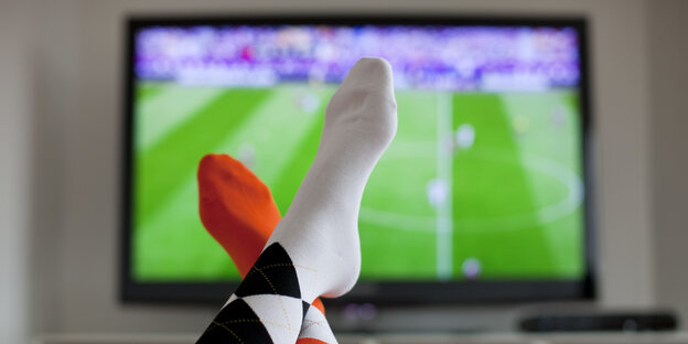 Zwei Füße vor einem Fernsehbildschrim. Im TV läuft Fußball Zwei Füße vor einem Fernsehbildschrim. Im TV läuft Fußball