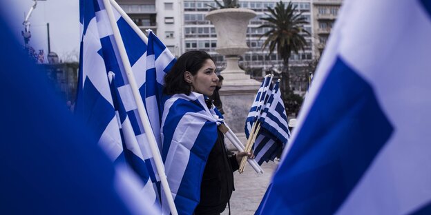 Eine Frau hält auf einer Demonstration sehr viele griechische Flaggen Eine Frau hält auf einer Demonstration sehr viele griechische Flaggen