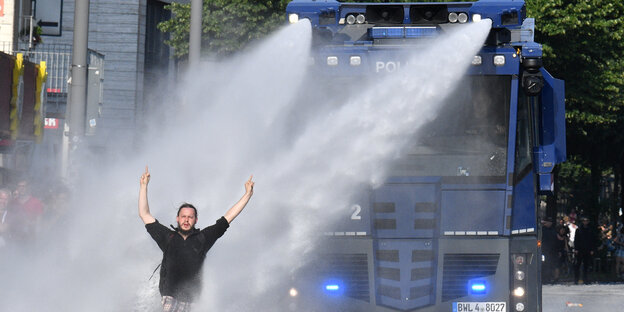 Ein Demonstrant mit schwarzem Kapuzenpulli steht vor einem blauen Wasserwerfer der Polizei, der im Einsatz ist Ein Demonstrant mit schwarzem Kapuzenpulli steht vor einem blauen Wasserwerfer der Polizei, der im Einsatz ist