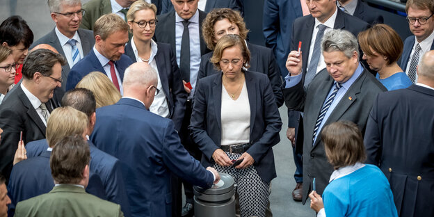 Viele Menschen stehen um einen Behälter herum, in dem sie einzeln Zettel hineinwerfen Viele Menschen stehen um einen Behälter herum, in dem sie einzeln Zettel hineinwerfen