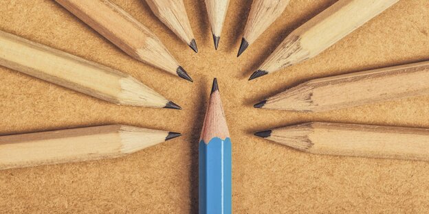 Viele Bleistifte mit braunem Lack gruppieren sich um einen Bleistift mit blauem Lack auf einer braunen Tischfläche Viele Bleistifte mit braunem Lack gruppieren sich um einen Bleistift mit blauem Lack auf einer braunen Tischfläche