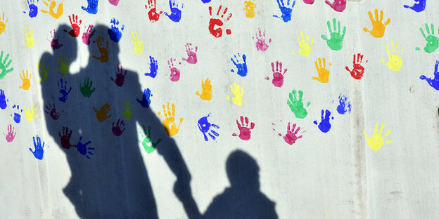 Schatten von Vater mit Kindern vor einer Wand, auf der lauter bunte Hände sind Schatten von Vater mit Kindern vor einer Wand, auf der lauter bunte Hände sind