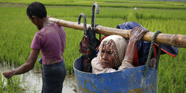 Flüchtlinge der Rohingya tragen eine alte Frau über einen schlammigen Weg, nachdem sie die Grenze zwischen Bangladesch und Myanmar überquert haben Flüchtlinge der Rohingya tragen eine alte Frau über einen schlammigen Weg, nachdem sie die Grenze zwischen Bangladesch und Myanmar überquert haben