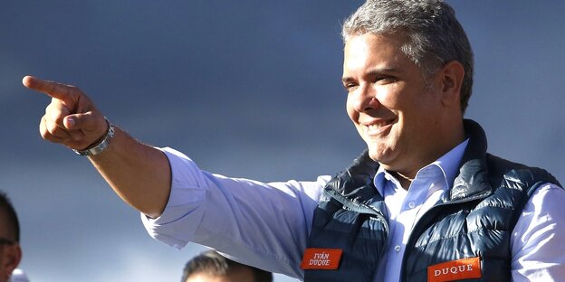 Iván Duque zeigt mit dem Zeigefinger nach links, im Hintergrund blauer Himmel